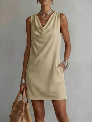 Sleeveless beige cowl neck mini dress with pockets and layered necklaces.