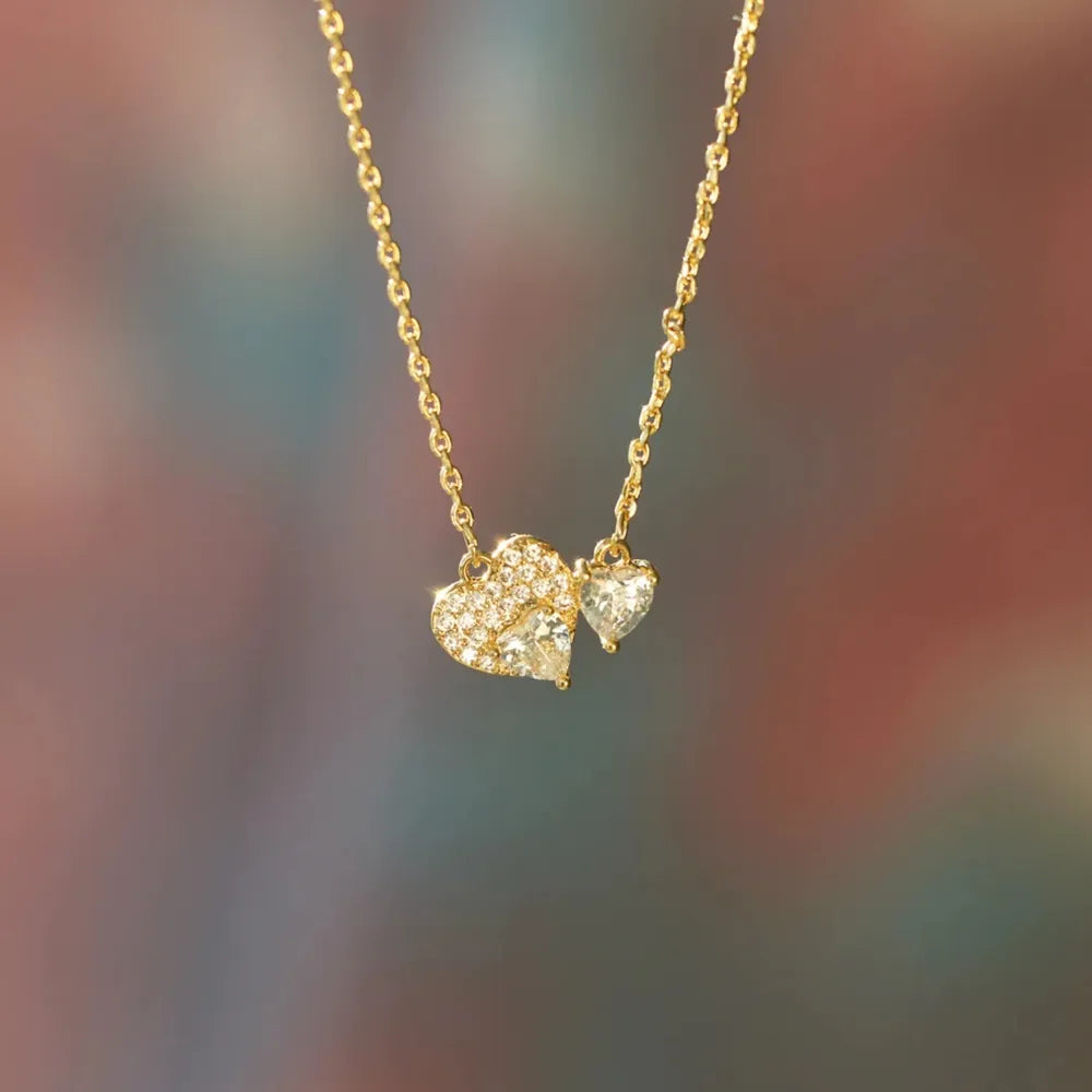 Gold chain necklace with two heart-shaped zirconia charms, one paved with small stones.
