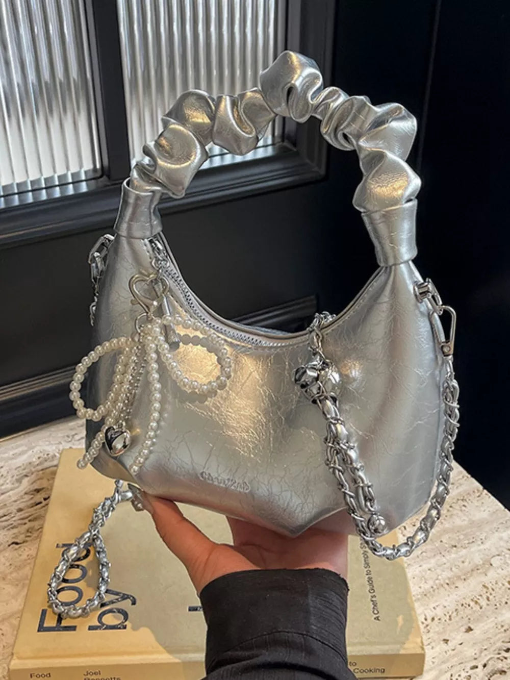 Silver ruched mini crossbody bag with pearl and heart pendant details and chain strap.