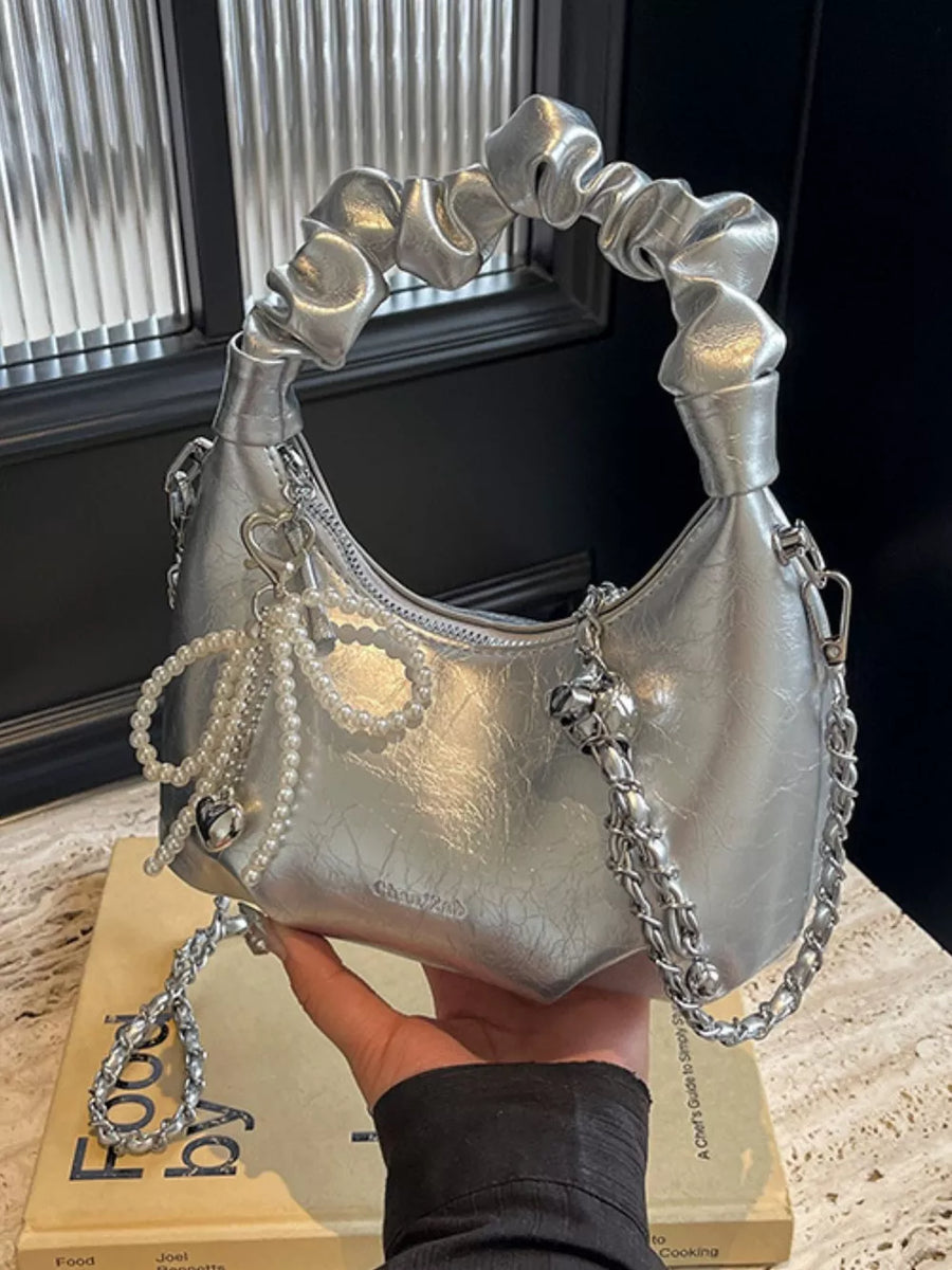 Silver ruched mini crossbody bag with pearl and heart pendant details and chain strap.