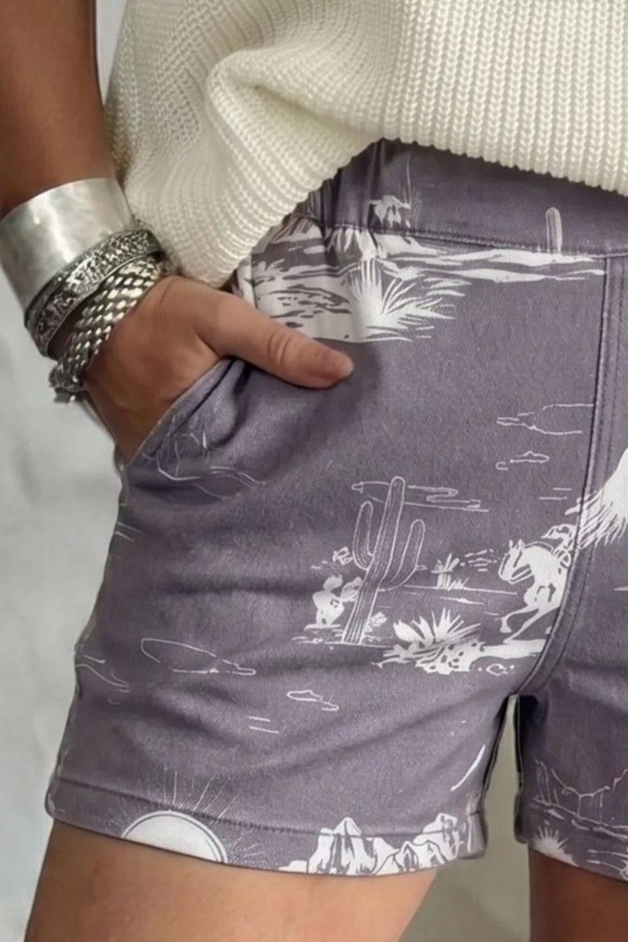 Denim shorts with western desert print, cacti, mountains and cowboy on horse.