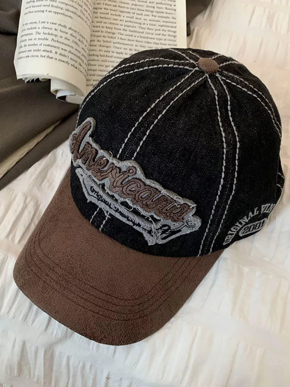 Distressed denim baseball cap in black with brown brim and embroidered "American" detail.