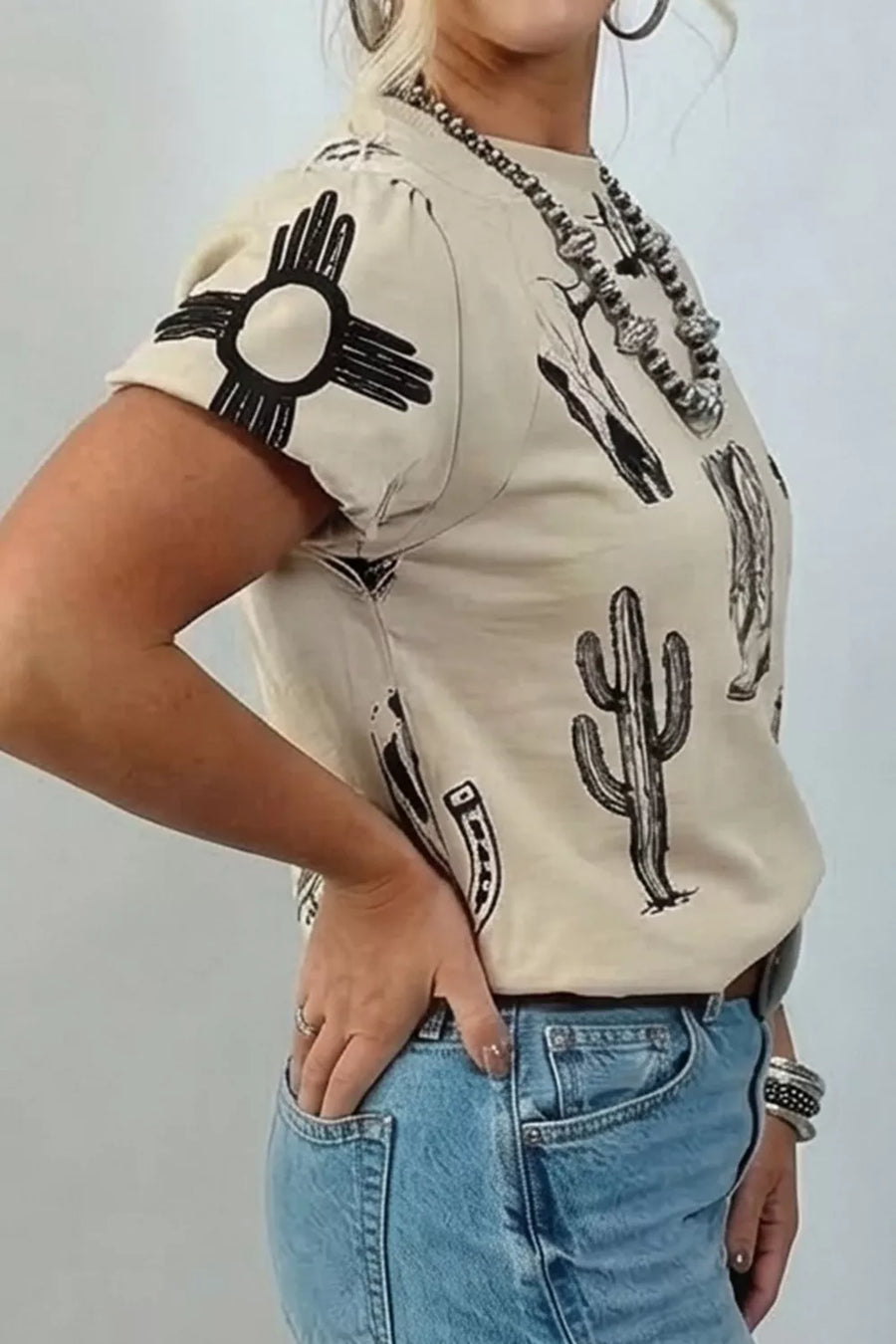 Cream crew neck t-shirt with western graphic print including sun symbol, cactus, and skull.