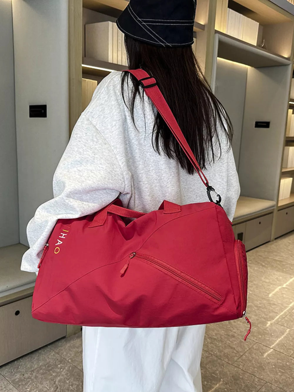 Red duffel bag with zippered pockets and embroidered logo, worn crossbody.