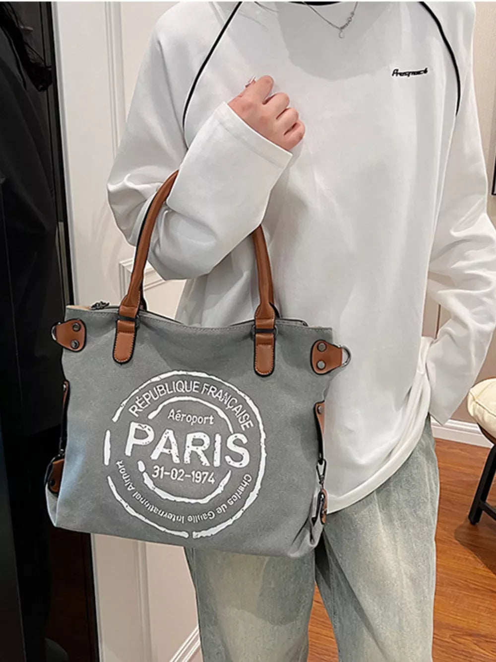 Parisian graphic tote bag in dark gray canvas with brown handles and airport stamp detail.