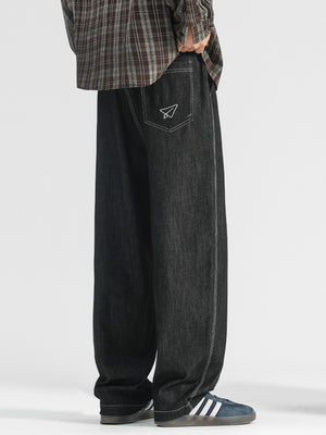 Men's black wide-leg jeans with paper airplane pocket detail and contrast stitching.
