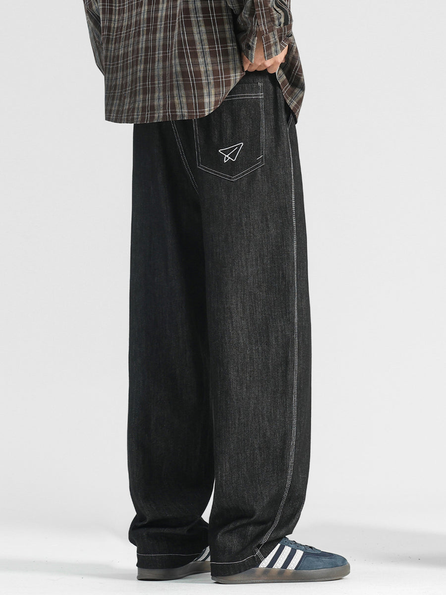 Men's black wide-leg jeans with paper airplane pocket detail and contrast stitching.