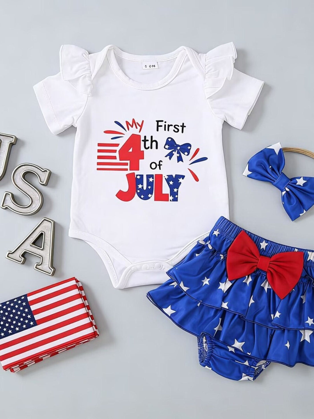 White baby onesie with ruffled sleeves and "My First 4th of July" graphic, paired with a star-print ruffled skirt and bow