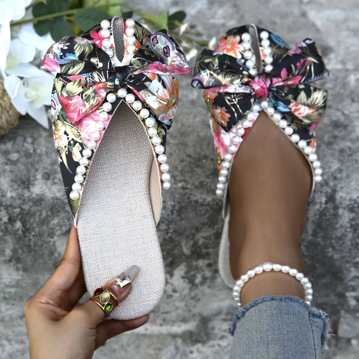 Floral bow pearl embellished slides with a black floral pattern.