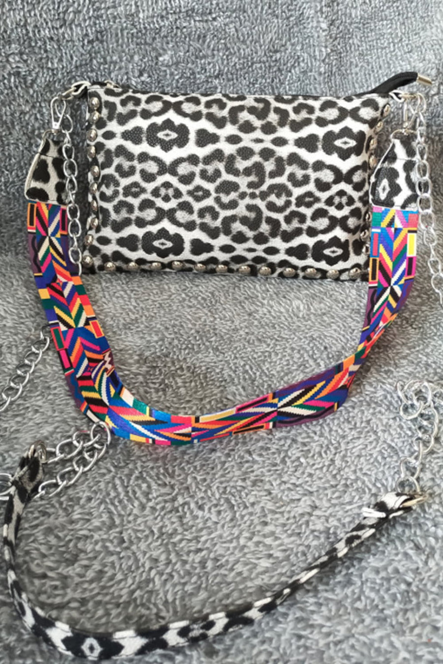 Leopard print studded shoulder bag with a colorful geometric strap and chain detail.