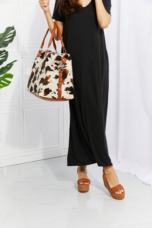 Cowhide print duffel bag with brown leather trim and straps.