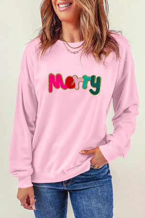 Blush pink crewneck sweatshirt with embroidered "Merry" text in colorful letters and gold glitter trim.