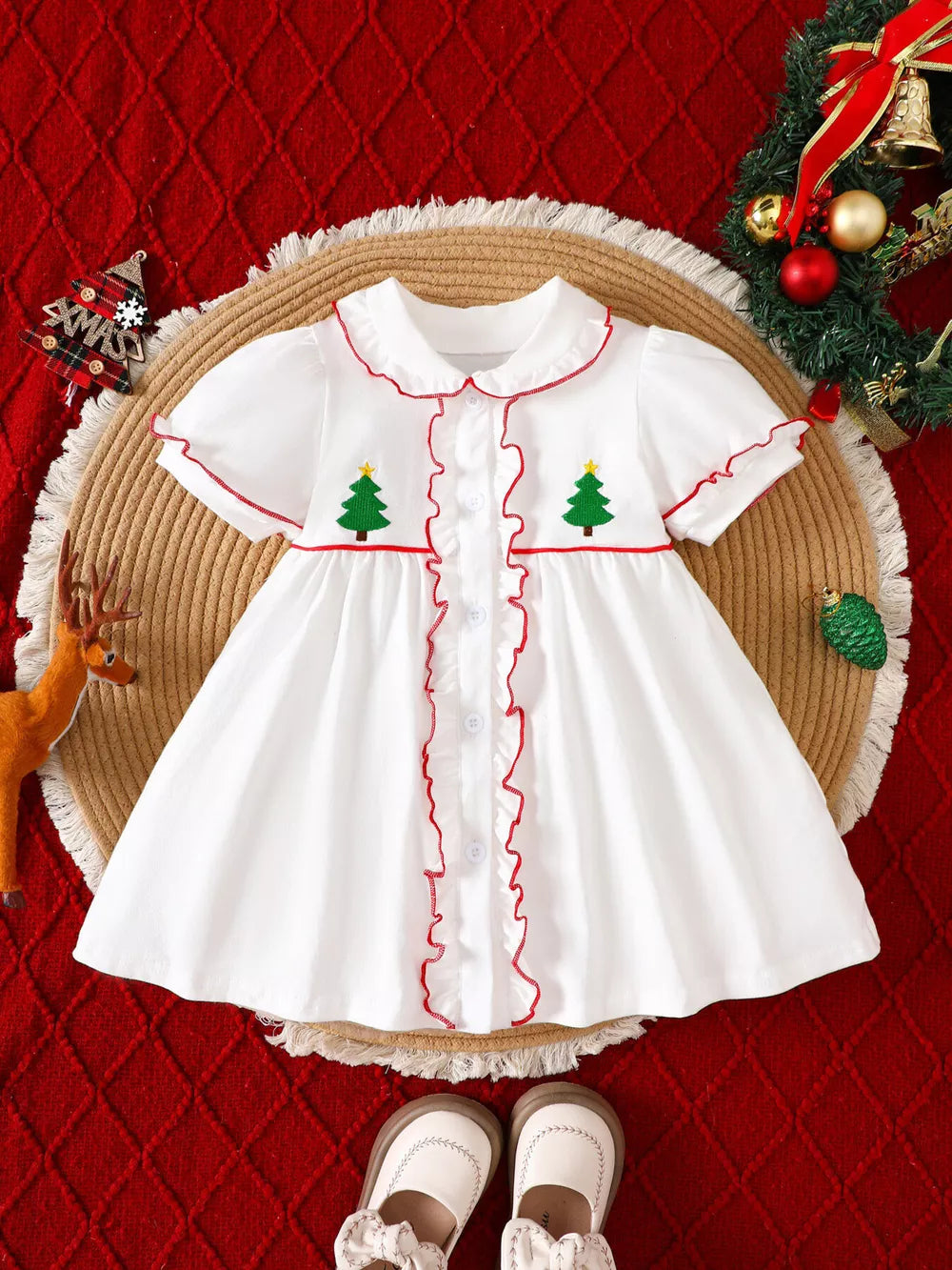 White baby dress with embroidered Christmas trees, red trim, and ruffles.