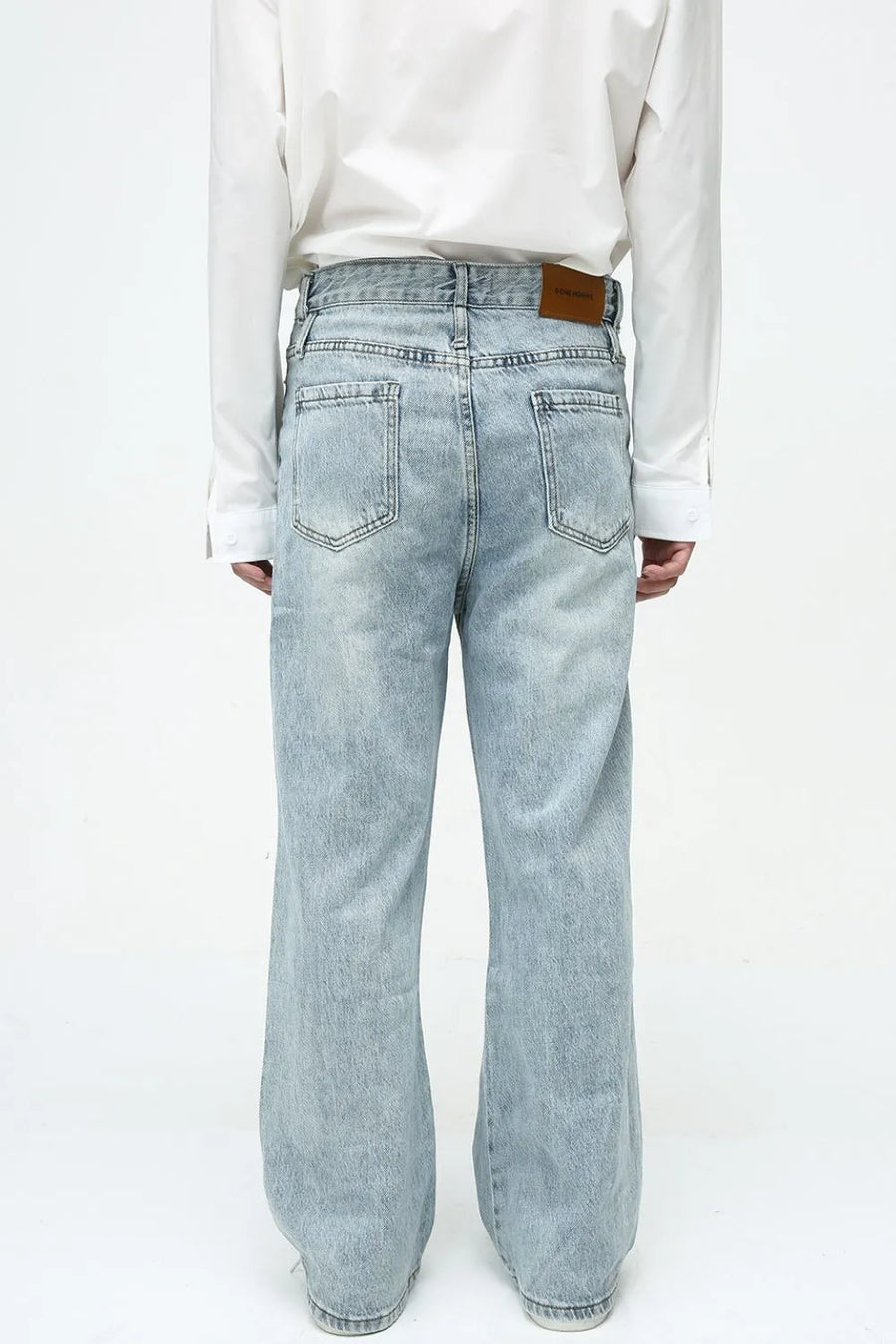 Light wash denim jeans with wide legs and vertical seams, featuring back pockets and a brown leather patch.