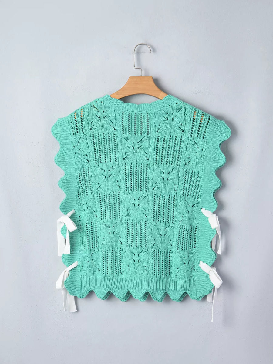 Green pointelle knit sweater with scalloped trim and side tie details.