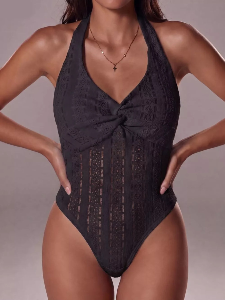 Black lace halter bodysuit with twisted front detail and intricate patterned cutouts.