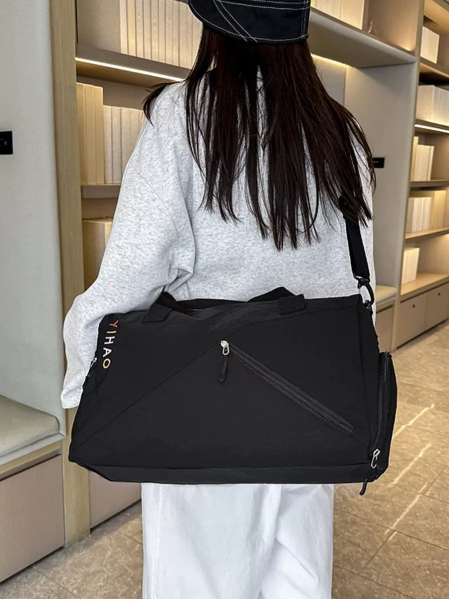 Black duffel bag with zippered compartments and colorful logo detail, worn crossbody.