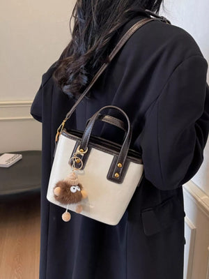 Mini leather crossbody bag in beige with brown trim and a fuzzy charm.