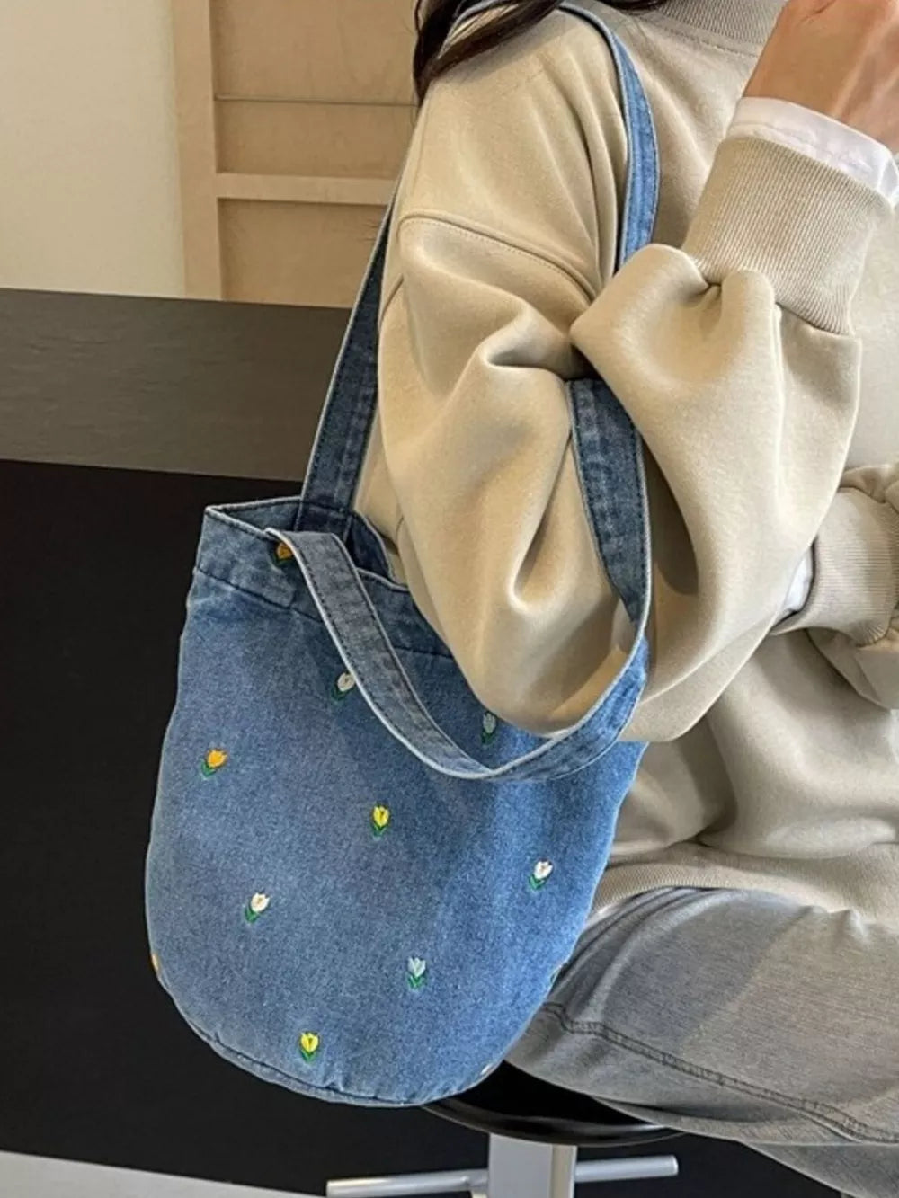 Denim tote bag with small embroidered white and yellow flowers.