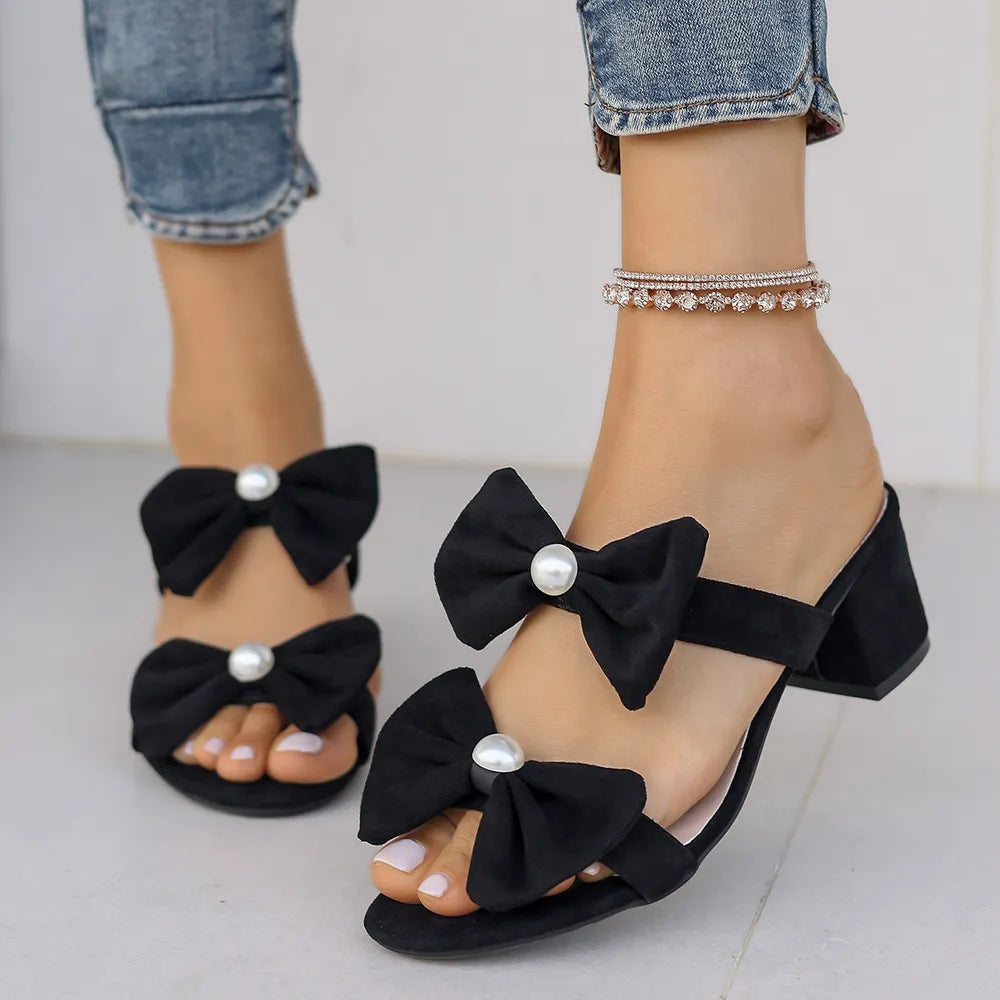 Black pearl-embellished bow block heel mules with open toe and ankle strap.