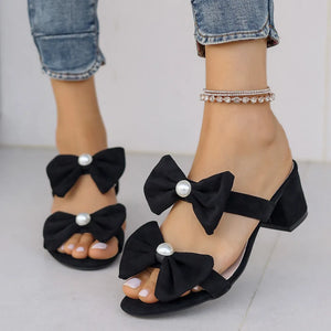Black pearl-embellished bow block heel mules with open toe and ankle strap.
