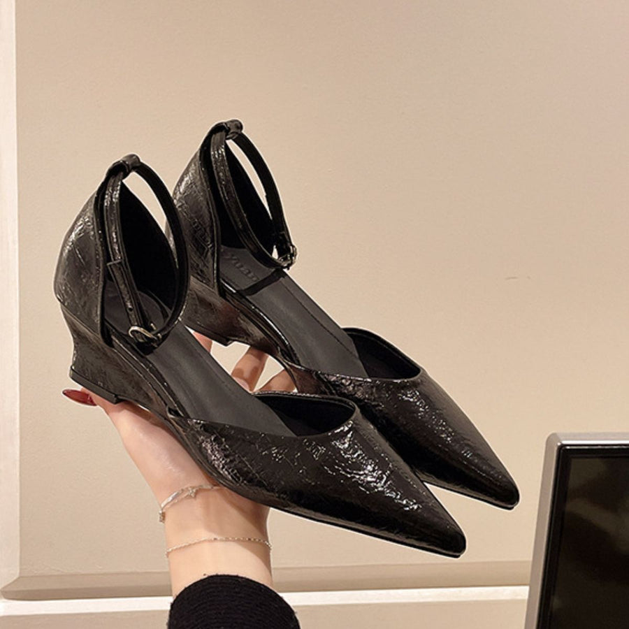 Black pointed-toe ankle strap wedge heels with adjustable buckle.