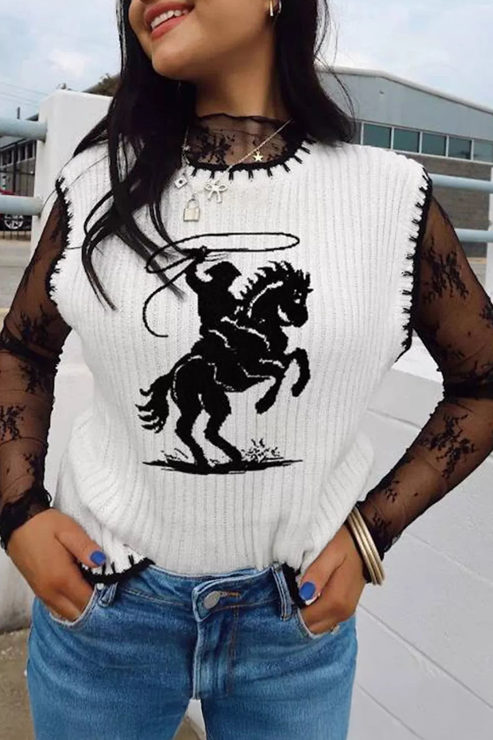 White knit sweater vest with contrast trim and rodeo graphic, worn over lace sleeves.