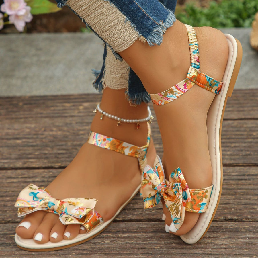 Floral bowknot flat sandals with colorful print and elastic ankle strap.