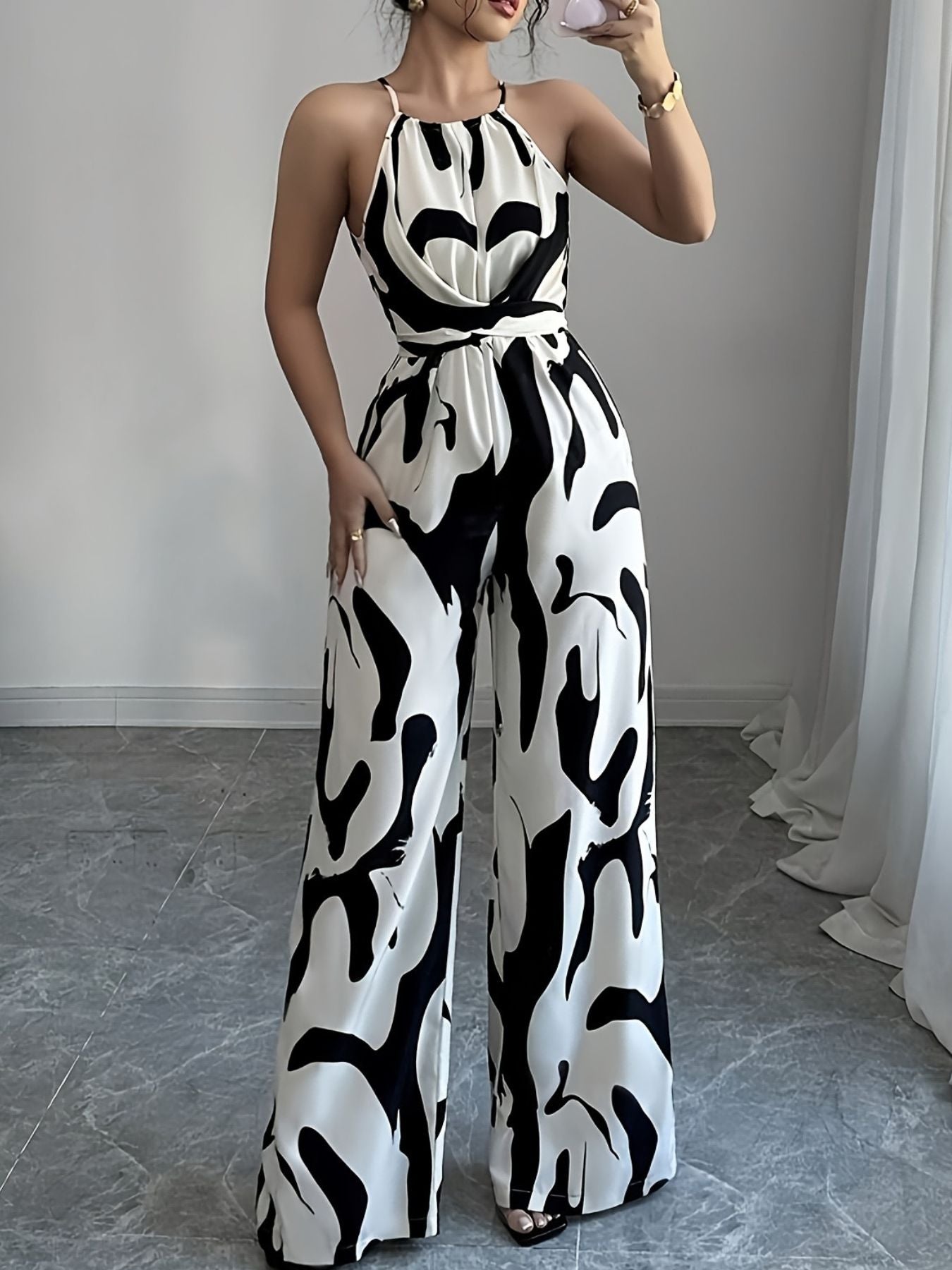 Elegant wide-leg jumpsuit with abstract black and white print, halter neck, and tie waist.