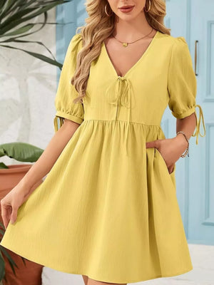 Yellow mini dress with puff sleeves, tie neck, and pockets.