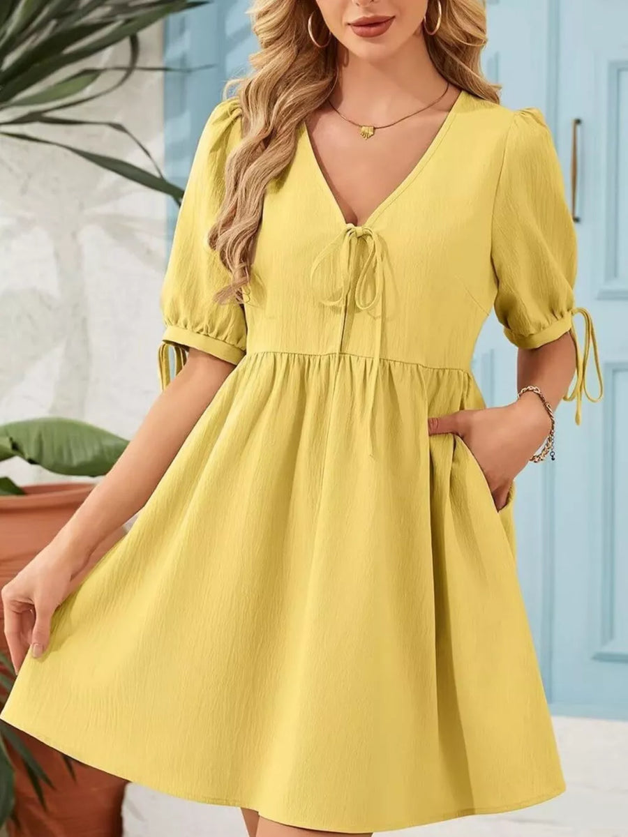 Yellow mini dress with puff sleeves, tie neck, and pockets.