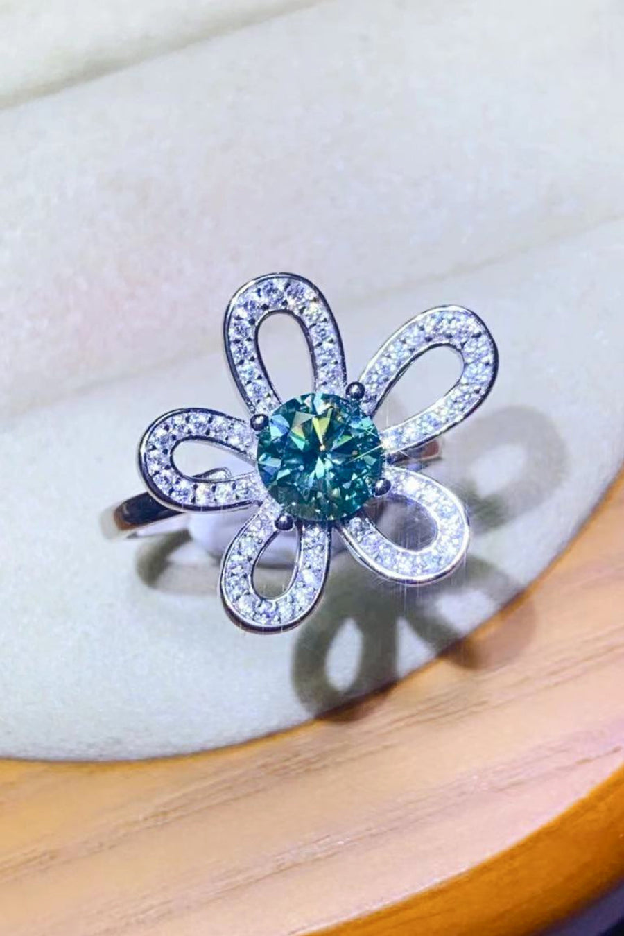 Teal moissanite flower ring with diamond accents.