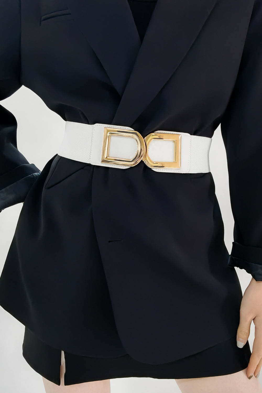 White elastic belt with double gold buckle detail cinching a black blazer.