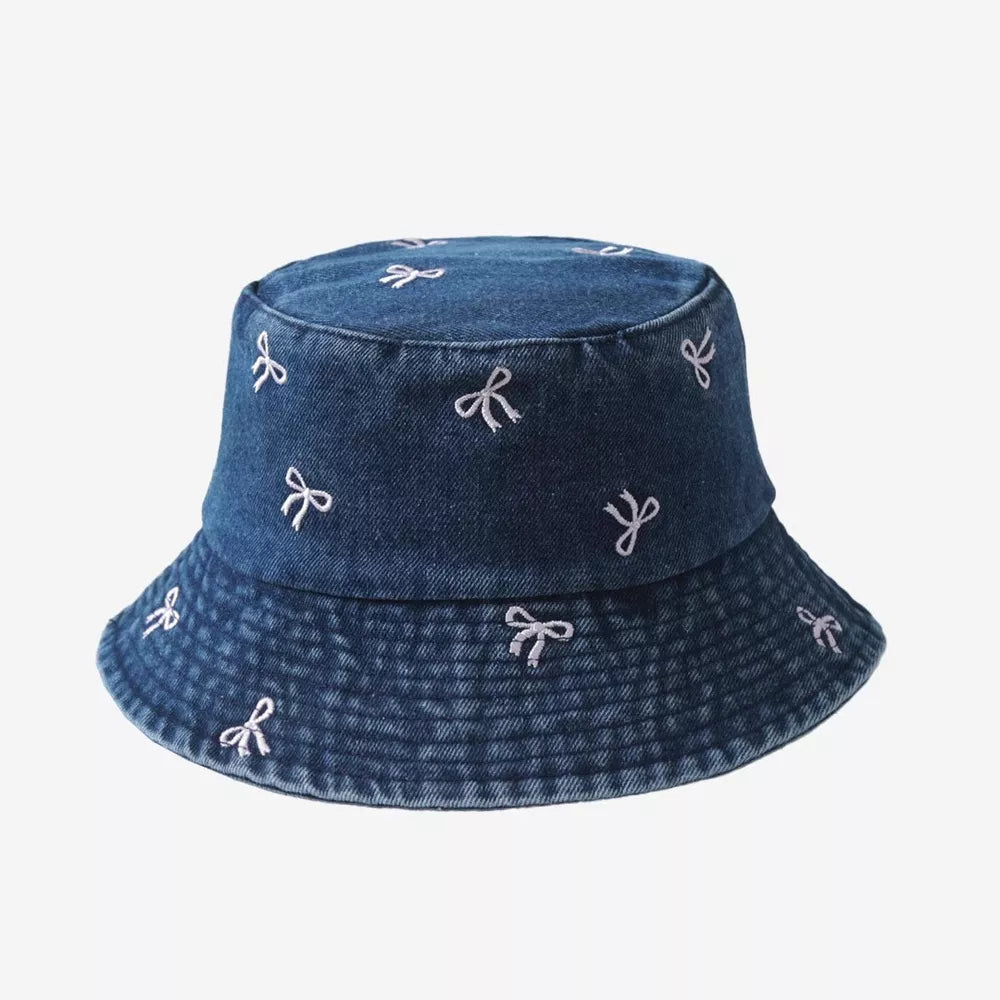 Denim bucket hat with all-over white bow embroidery and stitched brim detail.