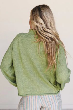 Green knit sweater with mock neck and long sleeves, styled with striped pants.