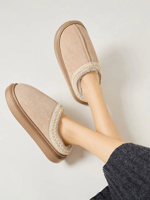 Tan shearling house slippers with embroidered trim and faux fur lining.