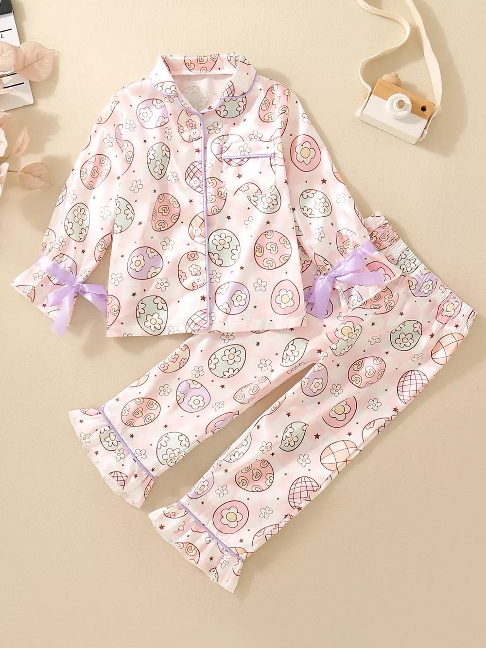 Toddler pink button-down pajama set with pastel egg print and purple trim.