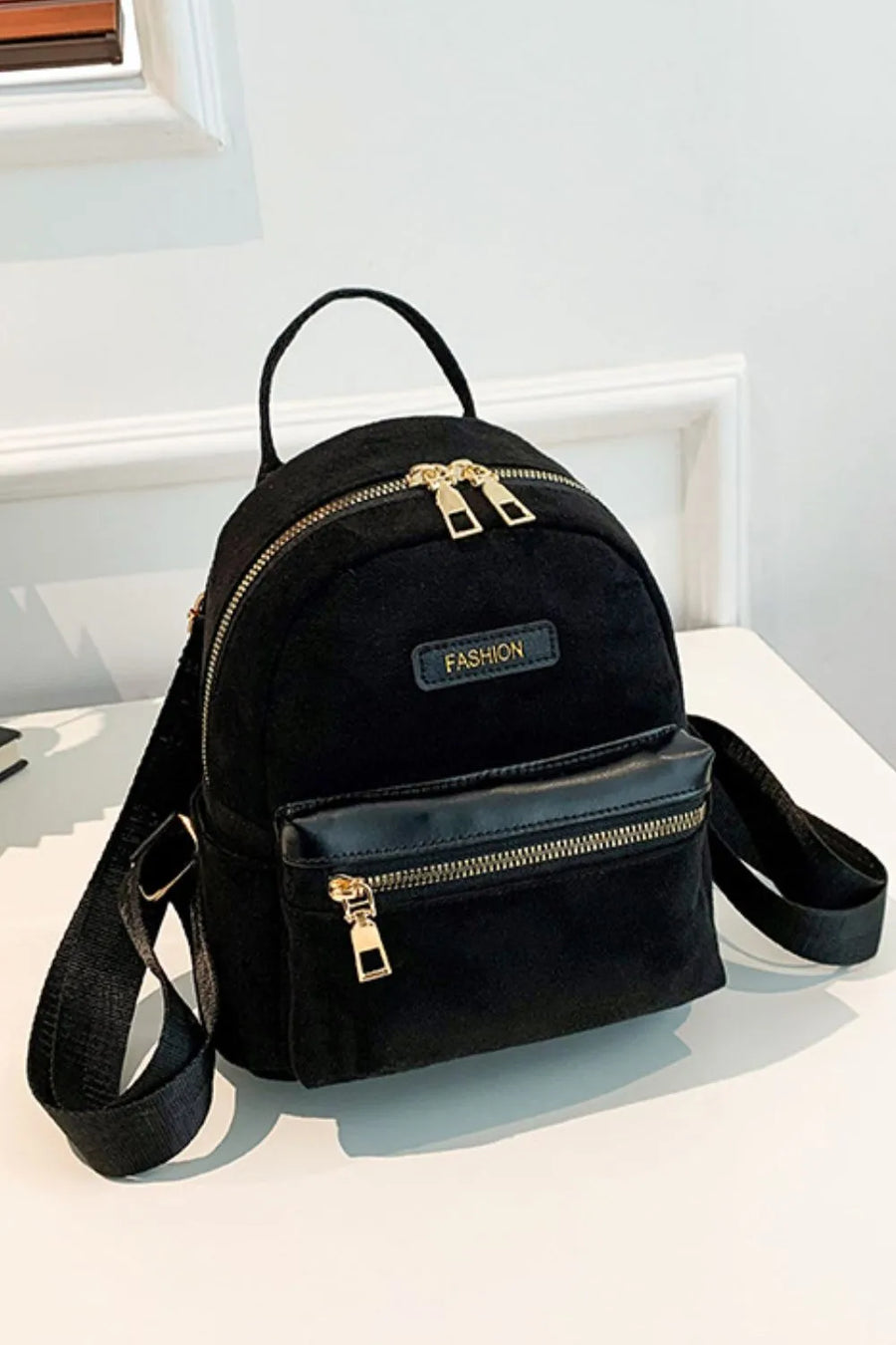 Black suede mini backpack with golden zips and "FASHION" detail