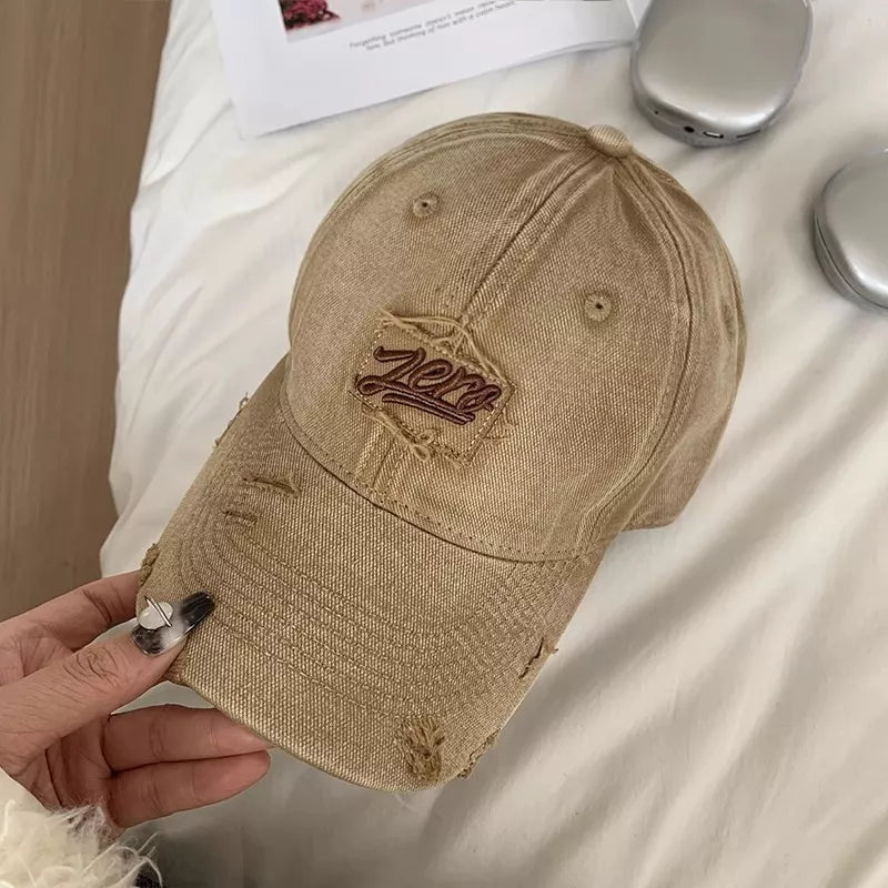 Distressed cotton baseball cap in beige with embroidered logo patch and frayed details.