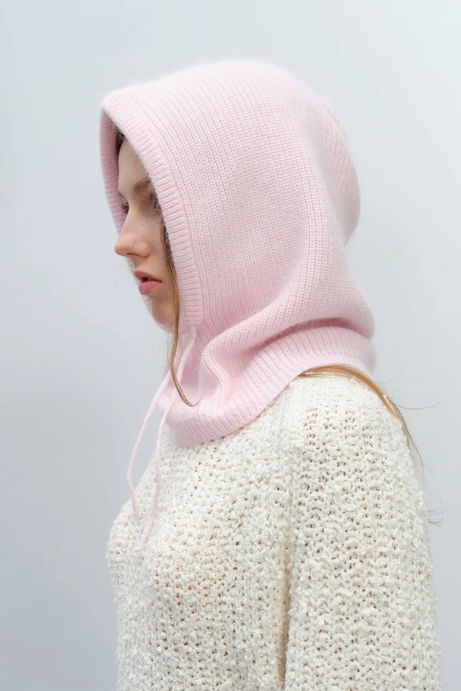 Hooded knit balaclava in blush pink with drawstring detail, worn by a model.