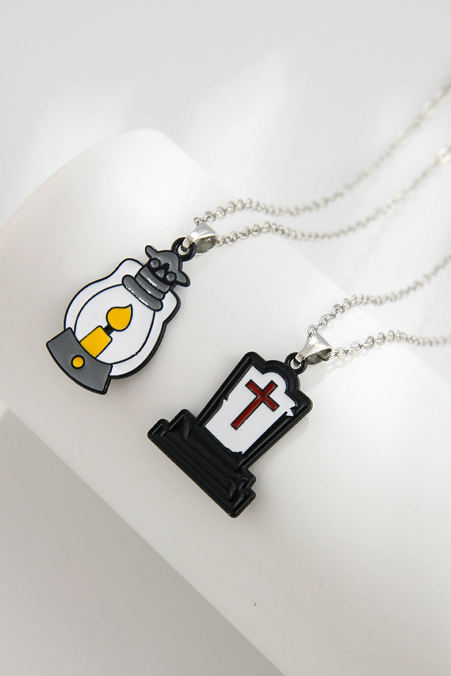 Spooky Season enamel pendant necklaces, one a lantern with yellow flame, one a tombstone with red cross.
