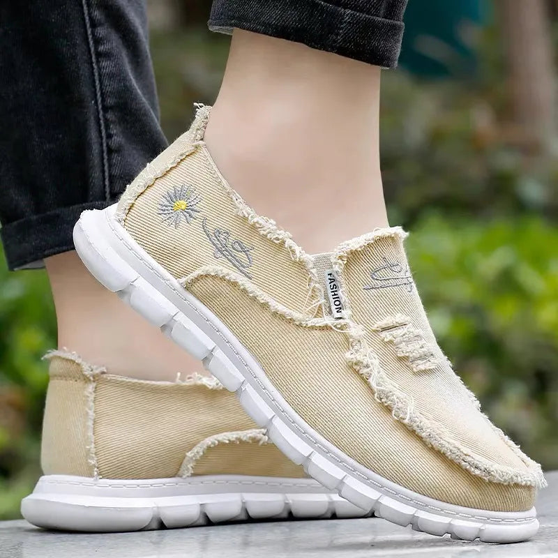 Khaki canvas slip-on shoes with raw edges and embroidered daisy detail.