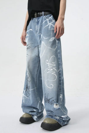 Graffiti art oversized denim trousers in medium wash with distressed details and white graphic print.