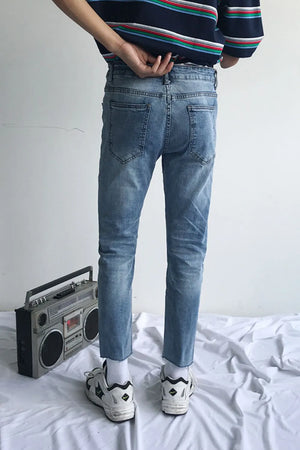 Medium wash denim jeans with raw hem and slim fit, styled with sneakers.