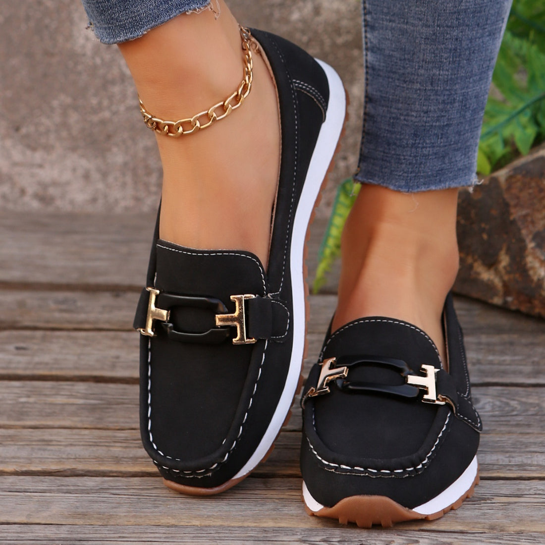 Black slip-on loafers with gold buckle detail and contrast stitching.