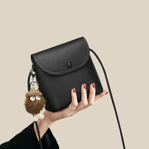 Black pebbled pu leather crossbody bag with button closure and fuzzy charm.