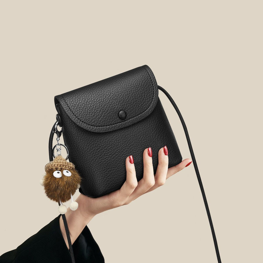Black pebbled pu leather crossbody bag with button closure and fuzzy charm.