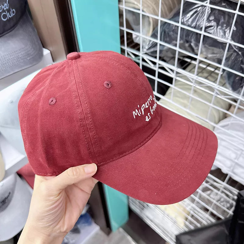 Red baseball cap with white embroidered "Mi perro es home" text detail