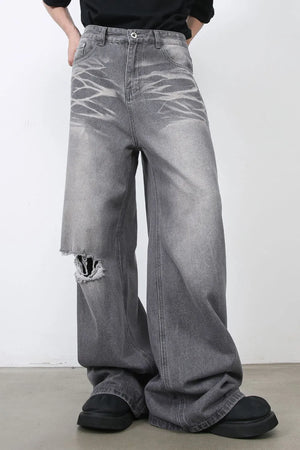 Dark gray distressed wide-leg jeans with a ripped knee and abstract faded pattern.