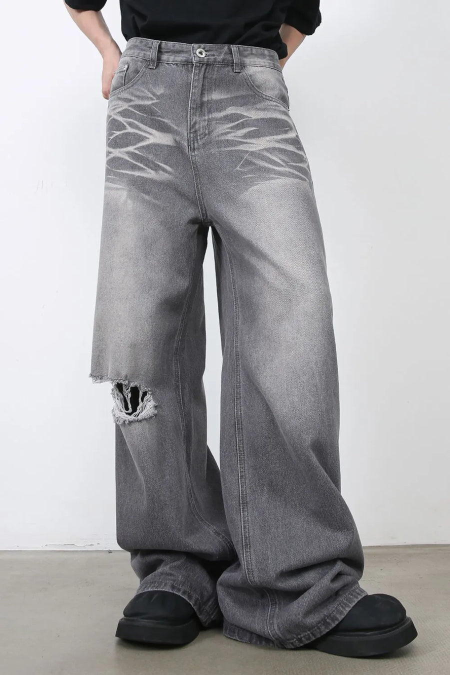 Dark gray distressed wide-leg jeans with a ripped knee and abstract faded pattern.